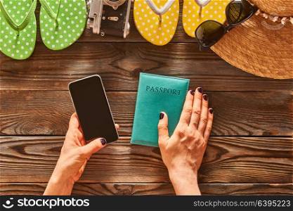 Planning a beach trip. Woman holding smartphone. Travel items for beach tourism still life over wooden background.