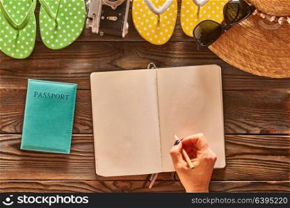 Planning a beach trip. Woman&rsquo;s hands with pencil over blank notebook. Travel items for beach tourism still life over wooden background.