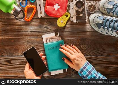 Planning a trip. Woman holding smartphone. Travel items for hiking tourism still life over wooden background