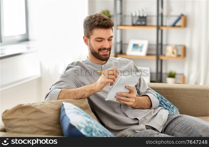 planning and people concept - smiling man writing to notebook at home. smiling man writing to notebook at home
