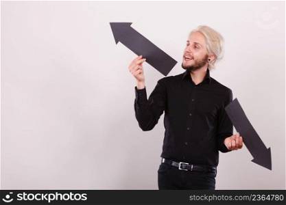 Planning, directions, choices concept. Man holding black arrow pointing left and right, opposite directions. Indoor shot on light background. Man holding black arrows pointing left and right