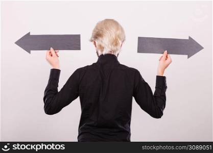 Planning, directions, choices concept. Man holding black arrow pointing left and right, opposite directions. Indoor shot on light background. Man holding black arrows pointing left and right