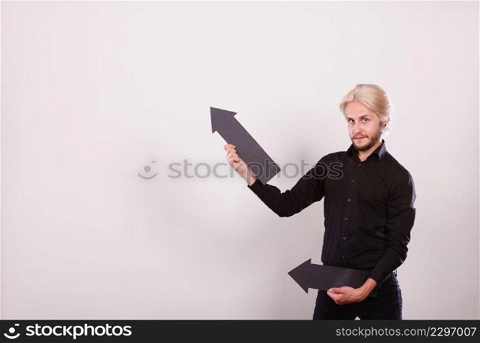 Planning, directions, choices concept. Man holding two black arrows pointing in the same directions. Indoor shot on light background. Man holding two arrows pointing same direction