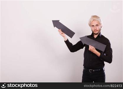 Planning, directions, choices concept. Man holding two black arrows pointing in the same directions. Indoor shot on light background. Man holding two arrows pointing same direction