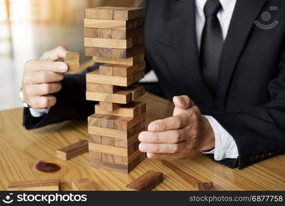 Planning, risk and wealth strategy in business concept, businessman and insurance gambling placing wooden block on a tower.