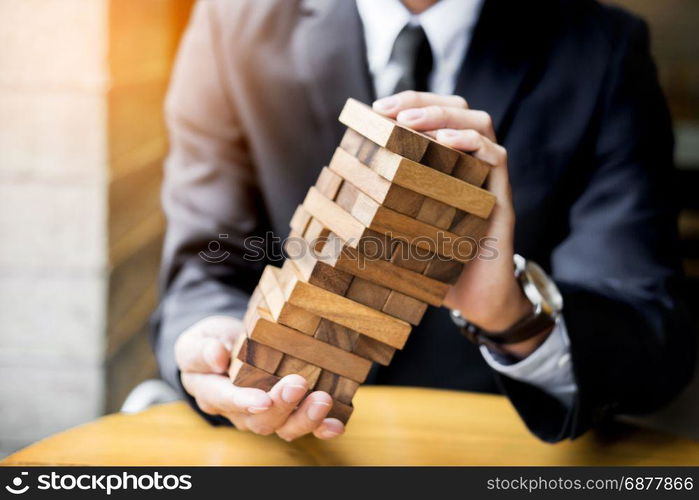 Planning, risk and wealth strategy in business concept, businessman and insurance gambling placing wooden block on a tower.