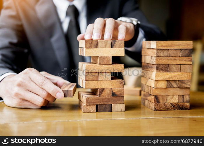 Planning, risk and wealth strategy in business concept, businessman and insurance gambling placing wooden block on a tower.