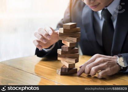 Planning, risk and wealth strategy in business concept, businessman and insurance gambling placing wooden block on a tower.