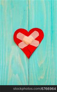 Plaster and paper broken heart on wooden background with copy-space