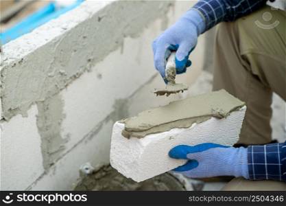 Plastering the wall.Hand holding a spatula with construction mix.Applying putty or tile glue to with lightweight concrete blocks.Plaster the wall with a putty knife.Internal construction,Construction concept.