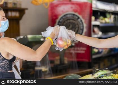 Plastic bag with fruits being passed from one woman to another, both using plastic gloves on an out of focus background. Safety and shopping concept.. Plastic bag with fruits being passed from one woman to another, both using plastic gloves.shopping concept