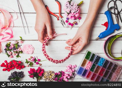 Plastic berries, flowers, beads and instruments for doing handmade headbands. Top view with hands