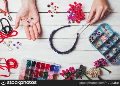 Plastic berries, flowers, beads and instruments for doing handmade headbands. Top view with hands