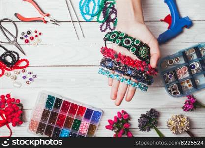 Plastic berries, flowers, beads and instruments for doing handmade headbands. Top view with hands