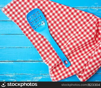 plastic blue spoon with holes on a red textile napkin, wooden background