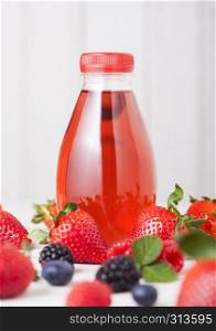 Plastic bottle of berries soda juice drink on wooden background with fresh strawberries and raspberries