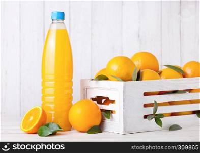 Plastic bottle of organic fresh orange juice with raw oranges in white wooden box