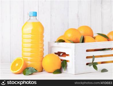 Plastic bottle of organic fresh orange juice with raw oranges in white wooden box