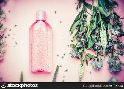 Plastic bottle with tonic or micellar cleansing water with fresh herbs and flowers on pink background, top view. Beauty, skin, hair or body care concept