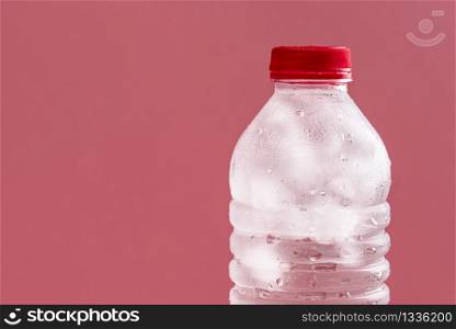 Plastic bottle with water and ice cubes close-up on a pink background. Cold natural water in a bottle. Fresh cold drink