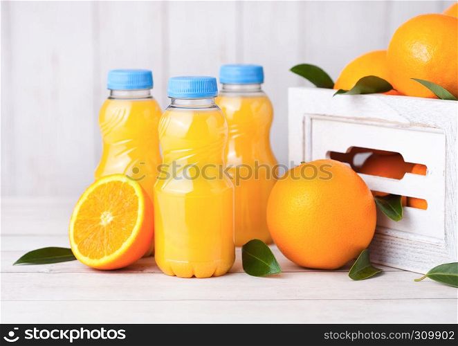 Plastic bottles of organic fresh orange juice with raw oranges in white wooden box