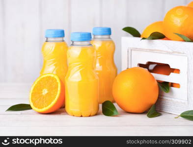 Plastic bottles of organic fresh orange juice with raw oranges in white wooden box