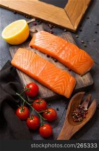 Plastic container with fresh salmon slice with oil tomatoes and lemon on stone kitchen background