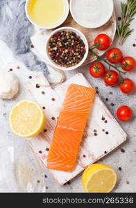 Plastic container with fresh salmon slice with oil tomatoes and lemon on stone kitchen background