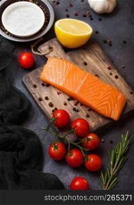 Plastic container with fresh salmon slice with pepper tomatoes and lemon on stone kitchen background