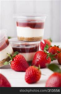 Plastic container with strawberry cream dessert on wooden background with fresh strawberries