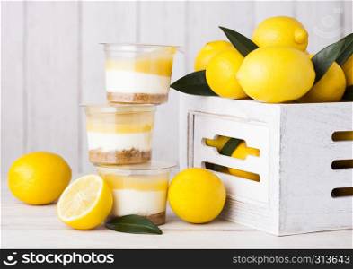 Plastic cup with lemon cream and biscuit dessert with raw lemons in white wooden box