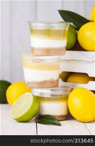Plastic cup with lemon lime cream and biscuit dessert with raw lemons in white wooden box