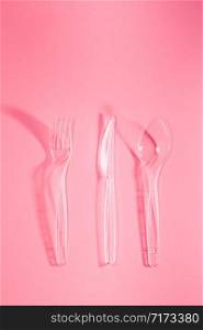 Plastic forks and knives scattered over pink background. Collecting plastic waste to recycling. Concept of plastic pollution and too many plastic waste. Copy space at the top