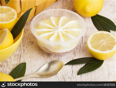 Plastic jar with lemon cheesecake mousse dessert with raw lemons in bamboo basket on light marblebackground