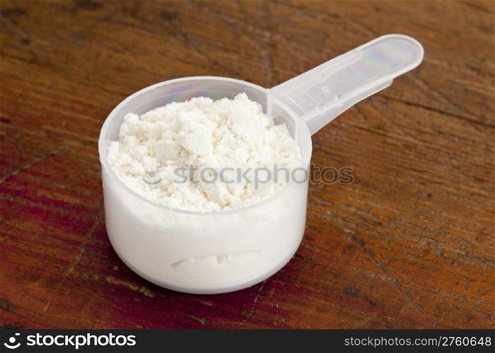 plastic measuring scoop of white powder (whey protein) against grunge wood background
