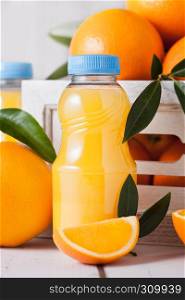 Plastic mini bottles of organic fresh orange juice with raw oranges in white wooden box