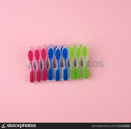 plastic multi-colored clothespins on a pink background, top view