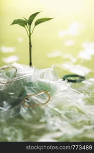 Plastic pollution problem concept with a young green weed growing from a pile of plastic trash, on a green background. Recycling waste concept.