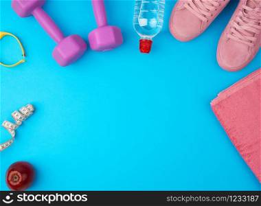 plastic purple dumbbells, sportswear, water, pink sneakers on a blue background, fitness kit, flat lay, copy space