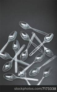 Plastic spoons scattered over black background. Collecting plastic waste to recycling. Concept of plastic pollution and too many plastic waste. Copy space at the top