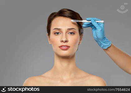 plastic surgery and beauty concept - beautiful young woman and hand with scalpel over grey background and snow. beautiful young woman and hand with scalpel