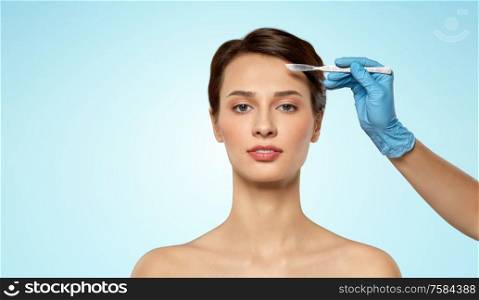 plastic surgery and beauty concept - beautiful young woman and hand with scalpel over blue background. beautiful young woman and hand with scalpel