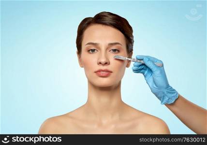 plastic surgery and beauty concept - beautiful young woman and hand with scalpel over blue background. beautiful young woman and hand with scalpel