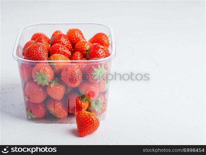 Plastic tray container of fresh organic healthy strawberries on stone kitchen table background.