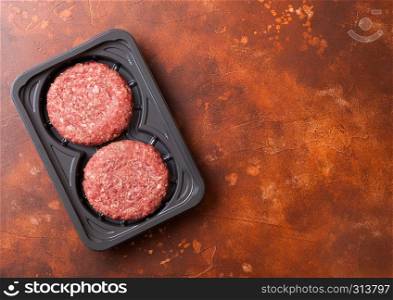 Plastic tray with raw minced homemade grill beef burgers with spices and herbs. Top view and space for text on rusty kitchen table background