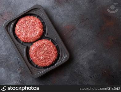Plastic tray with raw minced homemade grill beef burgers with spices and herbs. Top view and space for text on stone kitchen table background