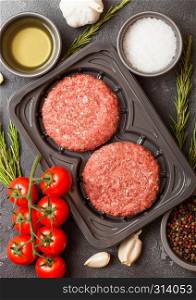 Plastic tray with raw minced homemade grill beef burgers with spices and herbs. Top view.