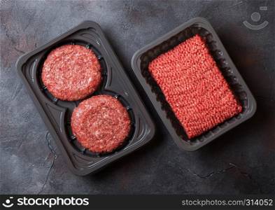 Plastic tray with raw minced homemade meat beef burgers with spices and herbs. Top view and space for text on stone kitchen table background