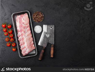 Plastic tray with raw pork ribs and vintage hatchets on wooden background. Fresh tomatoes and pepper with sea salt