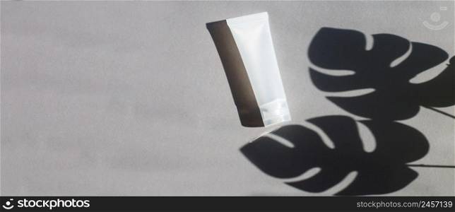 Plastic tube for cream or lotion on a gray background with a shadow of a montera leaves. Beauty concept.. Plastic tube for cream or lotion on a gray background with shadow of montera leaves. Beauty concept